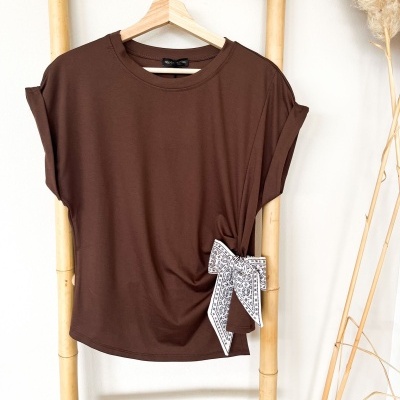 T-shirt castanha com laço estampado pendurada num suporte de bambu