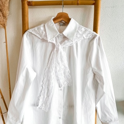 Camisa branca com renda floral pendurada num cabide numa escada de bambu