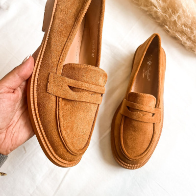 Mocassins de camurça caramelo com sola castanha clara sobre superfície branca.