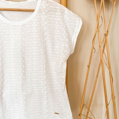 T-shirt branca com padrão floral bordado pendurada em cabide de madeira