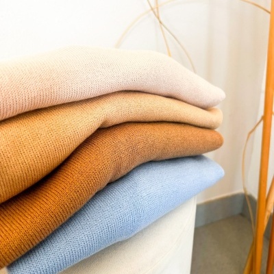 Pilhas de malhas em cores neutras e azul claro dobadas numa superfície branca