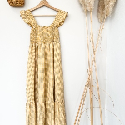 Vestido amarelo xadrez pendurado com vaso e flores secas ao lado