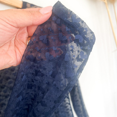 Mão segurando tecido de renda azul escura com padrão floral