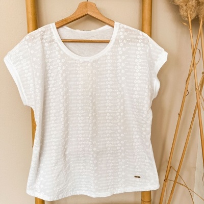 T-shirt branca feminina com padrão floral em relevo pendurada em cabide de madeira