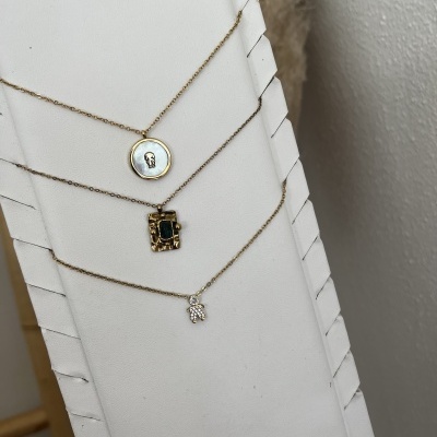 Colares dourados com diferentes pendentes expostos em suporte branco com textura.