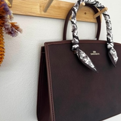 Mala castanha escura com alças cobertas por tecido branco com borboletas, pendurada em suporte de madeira
