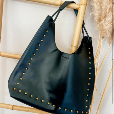 Mala vintage preta em pele com rebites dourados pendurada numa estrutura de madeira clara