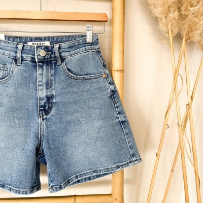 Calções de ganga azul claros pendurados em cabide de madeira numa estrutura de bambu.