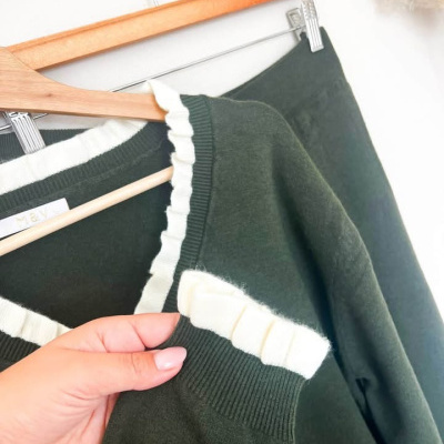 Conjunto de duas peças de malha verde escuro com detalhes em branco creme penduradas em cabides de madeira