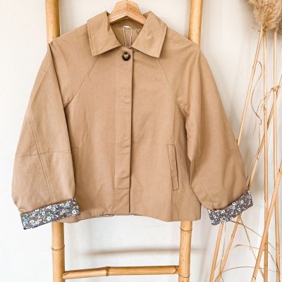 Casaco castanho claro com forro floral em cabide de madeira sobre escada de bambu