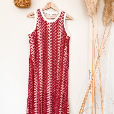 Vestido de malha com padrão em tons de vermelho, rosa e branco pendurado numa parede branca com suporte de madeira e cesta de vime