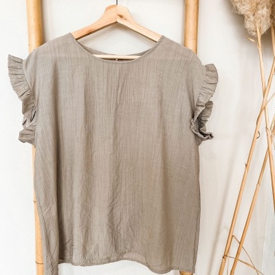 Blusa cinza clara com mangas folhadas pendurada num cabide de madeira