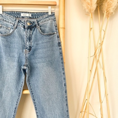 Calças de ganga azul claro penduradas em cabide de madeira com suporte de bambu e plantas secas ao lado