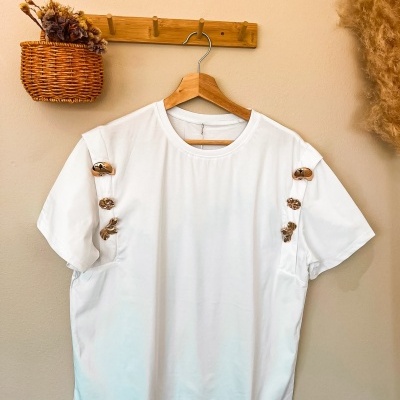 T-shirt branca com aplicações douradas pendurada em cabide de madeira
