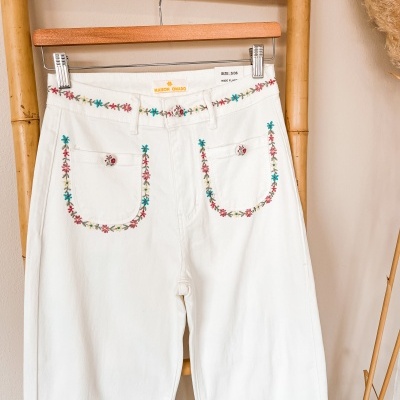 Calças brancas de ganga bordadas com flores coloridas penduradas em cabide de madeira