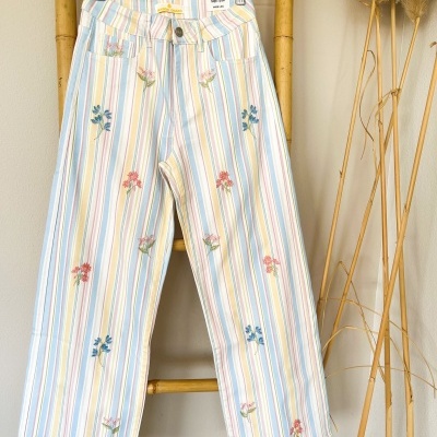 Calças compridas listradas com bordados de flores penduradas num cabide de madeira