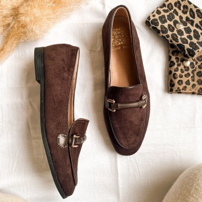 Par de mocassins castanhos aveludados com detalhe e fivela dourada, marcados GUAPISSIMA, perto de padrão leopardo.