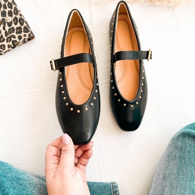 Sapatilhas pretas mary jane com tiras e tachas douradas sobre tecido claro