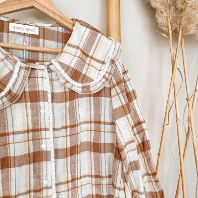 Camisa de algodão às riscas castanhas, brancas e bege com botões e gola com renda numa estrutura de madeira