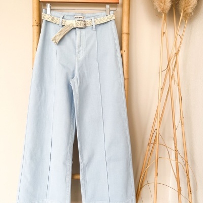 Calças largas azul claro com cinto bege penduradas numa estrutura de bambu