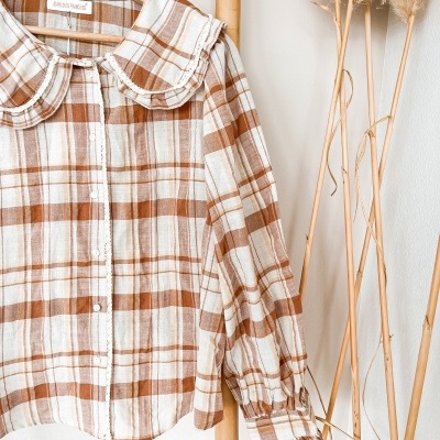 Blusa às riscas castanhas e creme com gola ampla e punhos franzidos pendurada em cabide de madeira