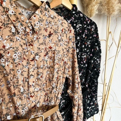 Vestidos camiseiros florais beige e preto pendurados em cabides de madeira com cinto castanho no vestido bege