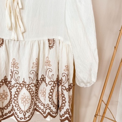 Roupa branca com bordados castanhos em padrão floral e geométrico