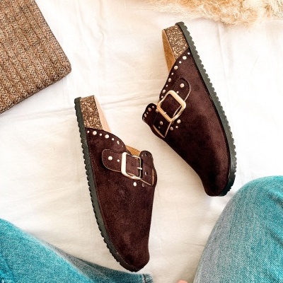 Sapatos mule em camurça castanha com fivela dourada e sola preta, sobre tecido branco