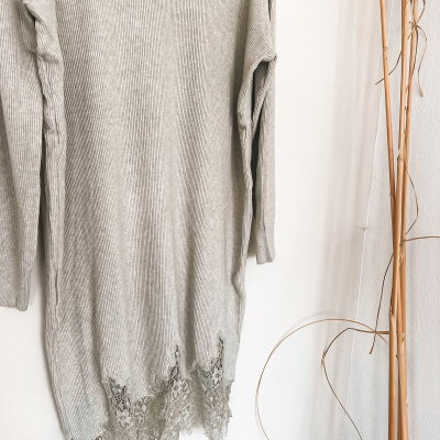 Vestido de malha cinzento com renda na bainha pendurado numa parede branca