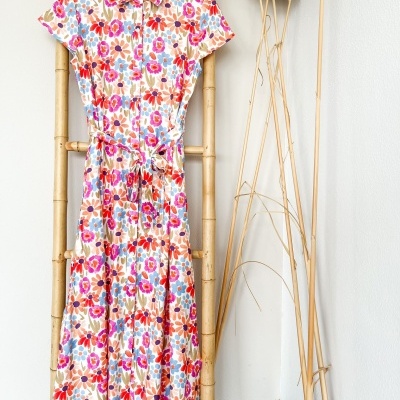 Vestido comprido floral com gola e cinto pendurado numa escada de bambu.