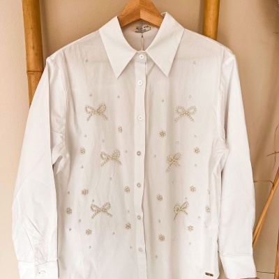 Camisa branca com laços e flores de pérolas pendurada num cabide de madeira