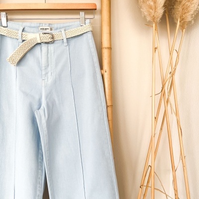 Calças de ganga azul claro com cinto bege penduradas em cabide de madeira e bambu