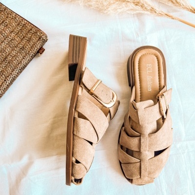 Sandálias beje de camurça com fivela dourada sobre fundo branco e bolsa de palha