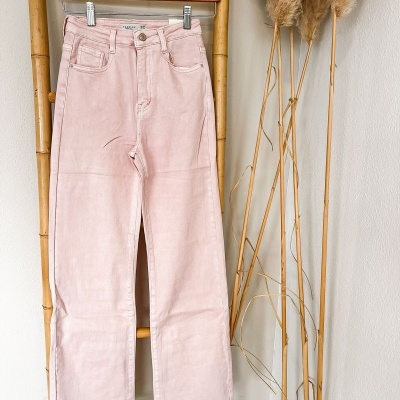 Calças cor de rosa de veludo penduradas numa estrutura de madeira com plantas secas ao lado