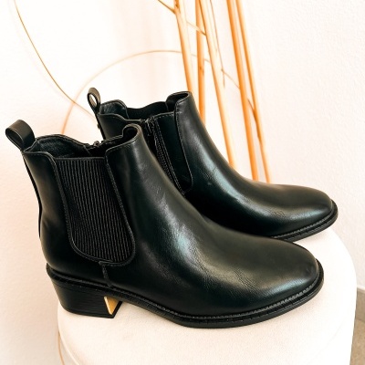 Botins pretos de couro com elásticos e salto baixo com detalhe dourado sobre superfície branca