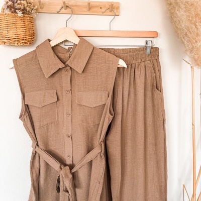 Conjunto de camisa sem mangas e calças castanhas pendurados em cabides de madeira