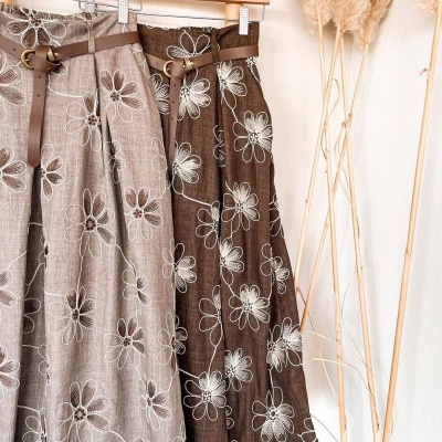 Dois vestidos florais midi bege e castanho pendurados com cintos e plantas secas ao lado