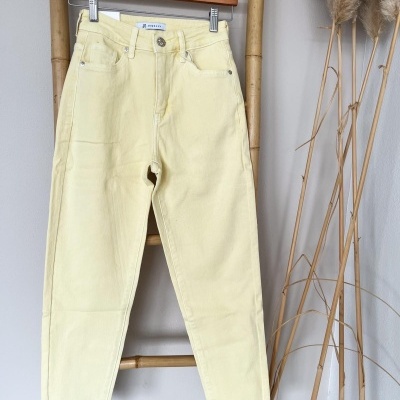 Calças de ganga amarelas claras penduradas em cabide numa estrutura de bambu