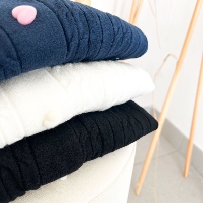 Três peças de roupa felpudas empilhadas em azul escuro, branco e preto.