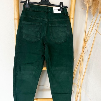 Calças verdes escuras penduradas em cabide numa estrutura de bambu