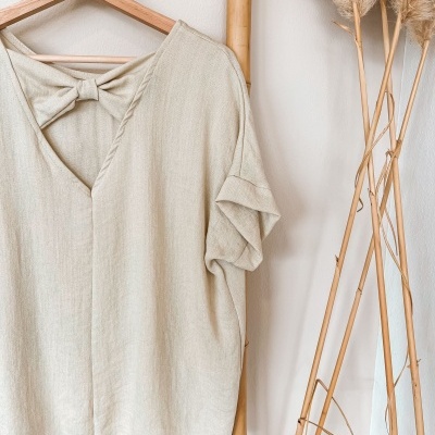 T-shirt bege com laço na gola pendurada em suporte de bambu