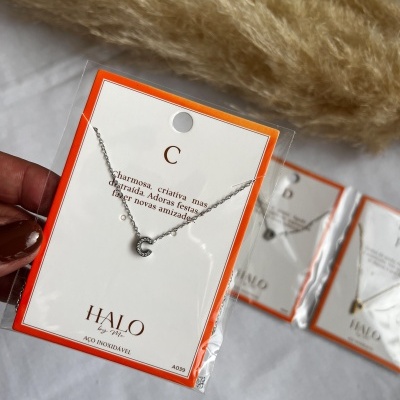 Colar com pendente letra C em embalagem com borda laranja e texto descritivo