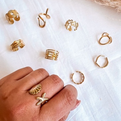 Conjunto de anéis dourados variados expostos sobre tecido branco com mão a usar anéis.
