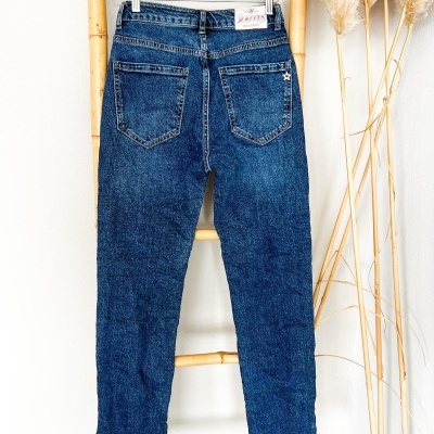 calças de ganga azuis penduradas numa estrutura de madeira com plantas decorativas ao lado