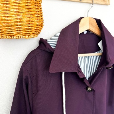 Casaco roxo pendurado numa cabide de madeira com interior riscado branco e cinza.