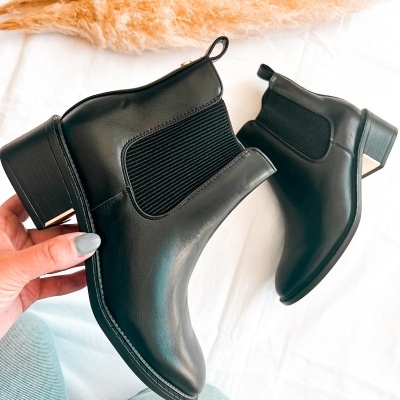 Botas Chelsea pretas com salto baixo e elástico lateral sobre tecido branco com flores secas