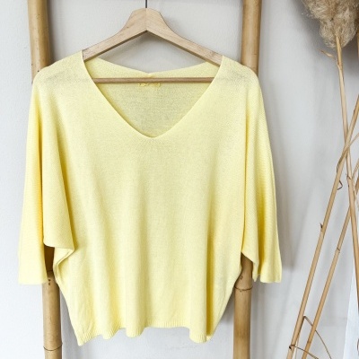 Camisola amarela clara com decote em V pendurada num cabide de madeira numa estrutura de bambu.