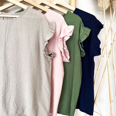 Quatro t-shirts com folhos em várias cores penduradas em cabides de madeira