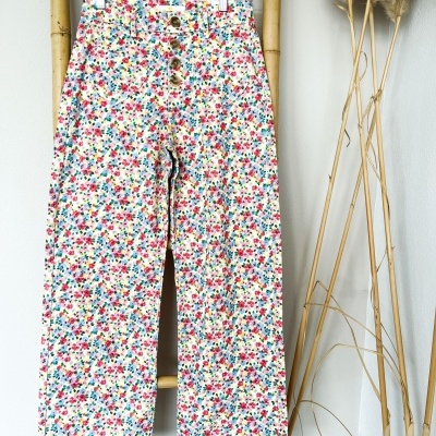 Calças florais multicoloridas penduradas em cabide de madeira e suporte de bambu