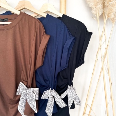 Três t-shirts de cores diferentes com laços nas mangas penduradas em cabides de madeira